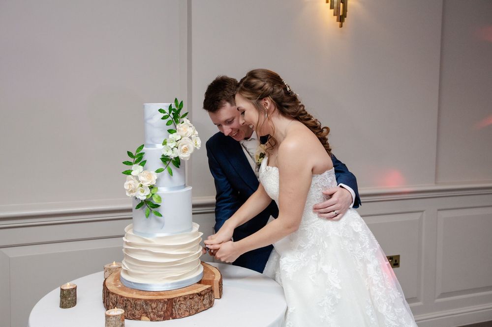 Four tiered baby blue and ivory wedding cake. Baby blue top tier is marbled. Bottom tier is ivory ruffles. Abi and Damian cutting their cake